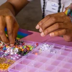 Hands sorting colorful beads into a compartment tray