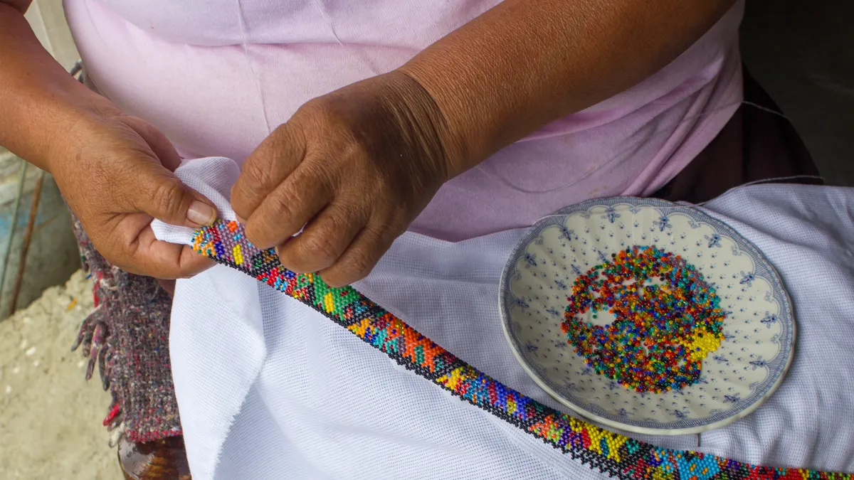 Hands stringing colorful beads beside a bowl of beads