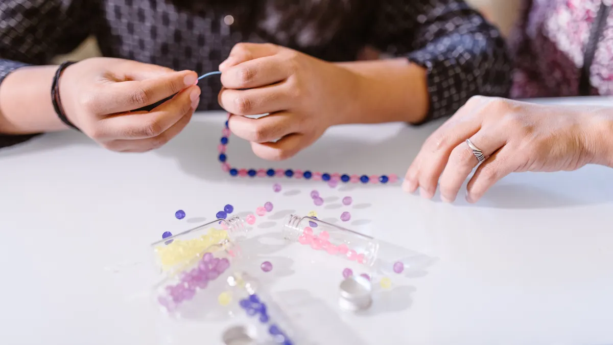 Hands making beaded bracelets at a craft table